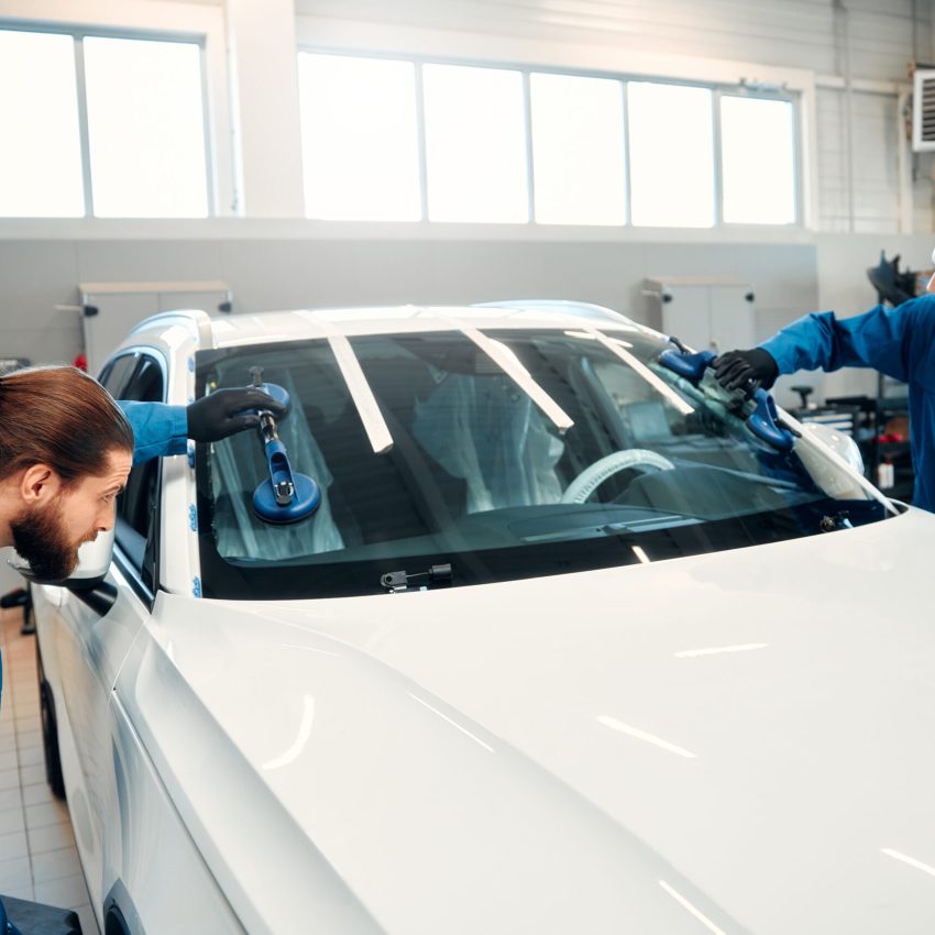 A professional mechanic changes a windshield on a car in a car workshop. Hands mechanic holding a tool. Replacement of automobile glasses.