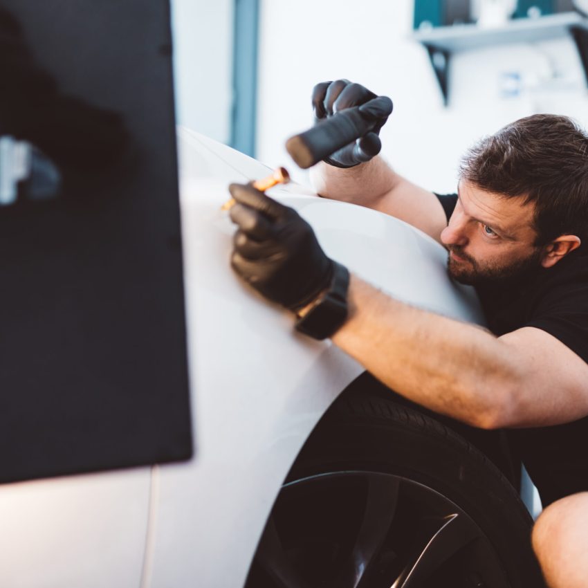 Car mechanic working to remove dent in workshop. Professional car detailing service